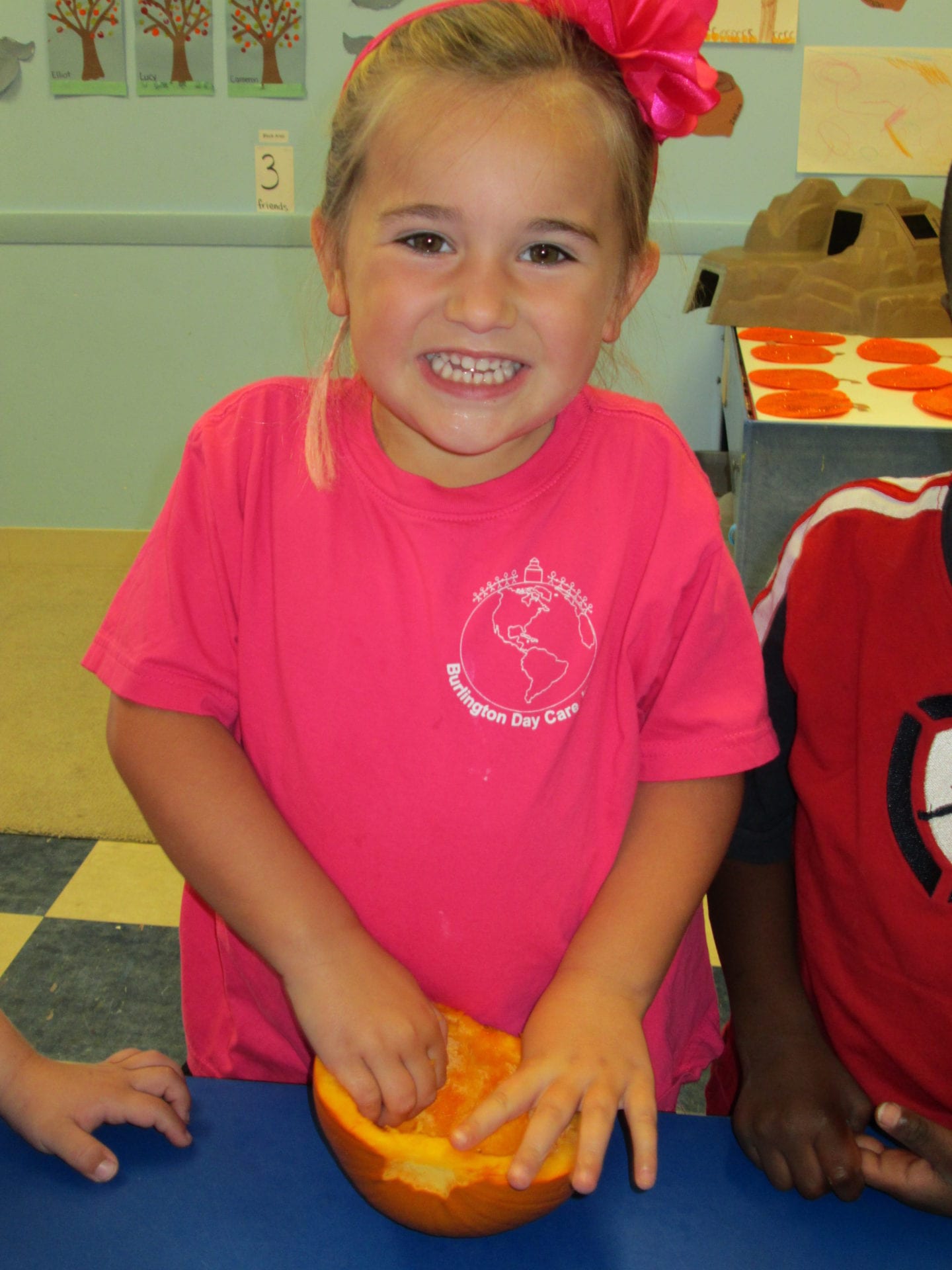 A little girl in pink shirt holding an orange.